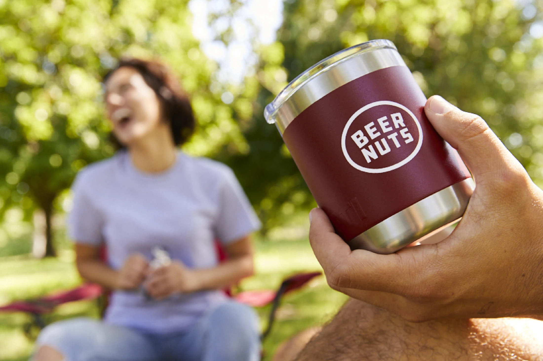 A woman holding a Beer Nuts yeti mug in a park.
