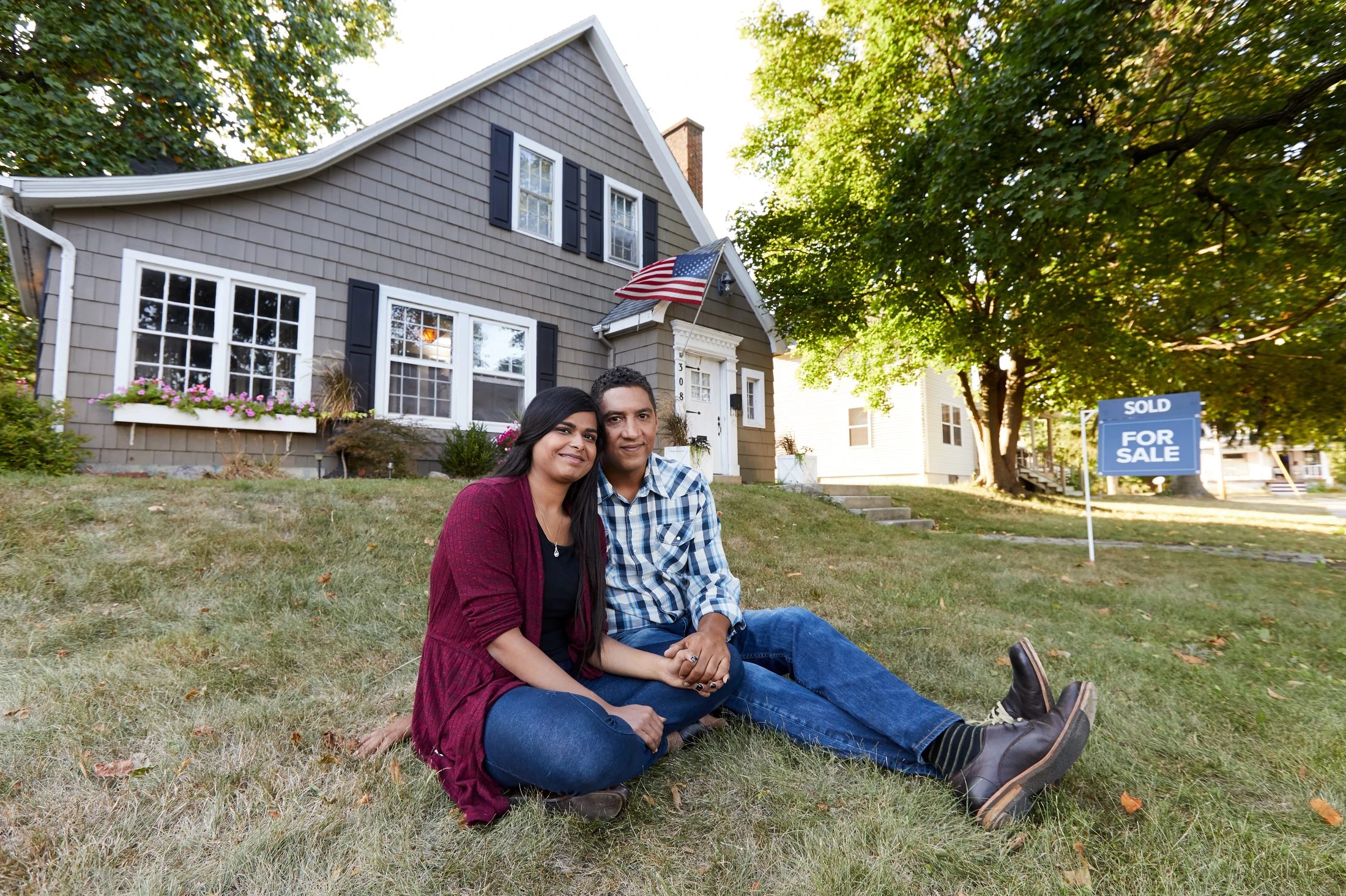 A couple sitting on the grass in front of their house.