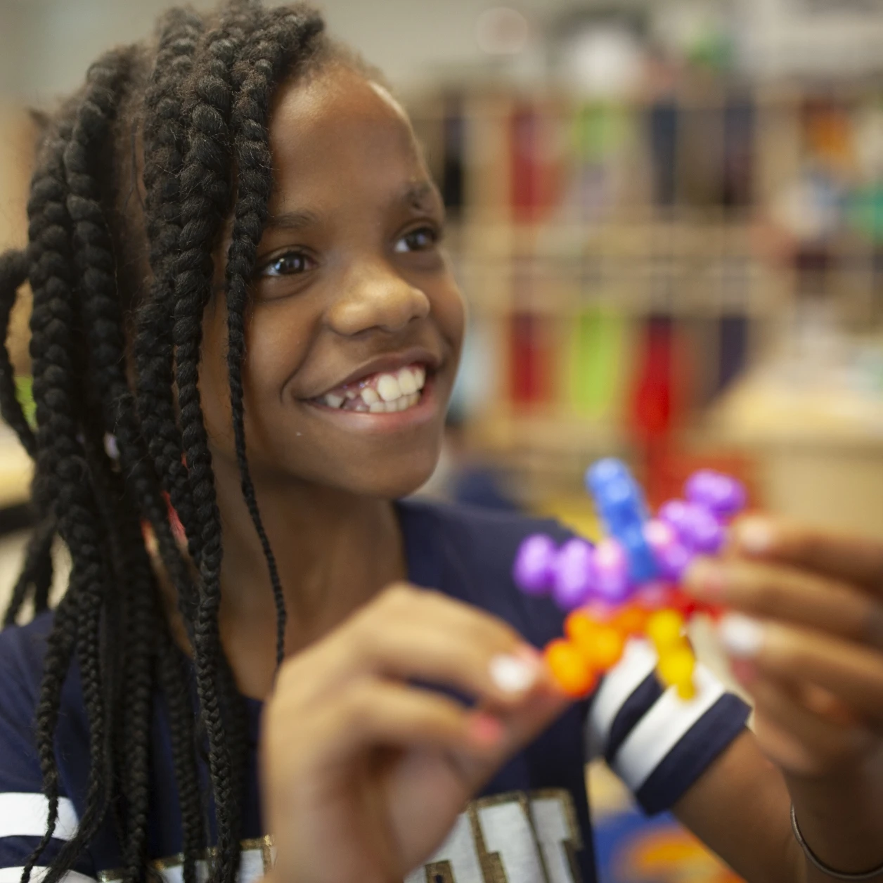 A young girl smiles while playing with colorful blocks in a classroom.