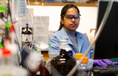 A woman in a scientific overcoat with various scientific equipment in the foreground.
