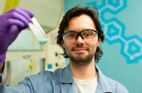 A man in scientific apparel holding a test tube and looking at the camera