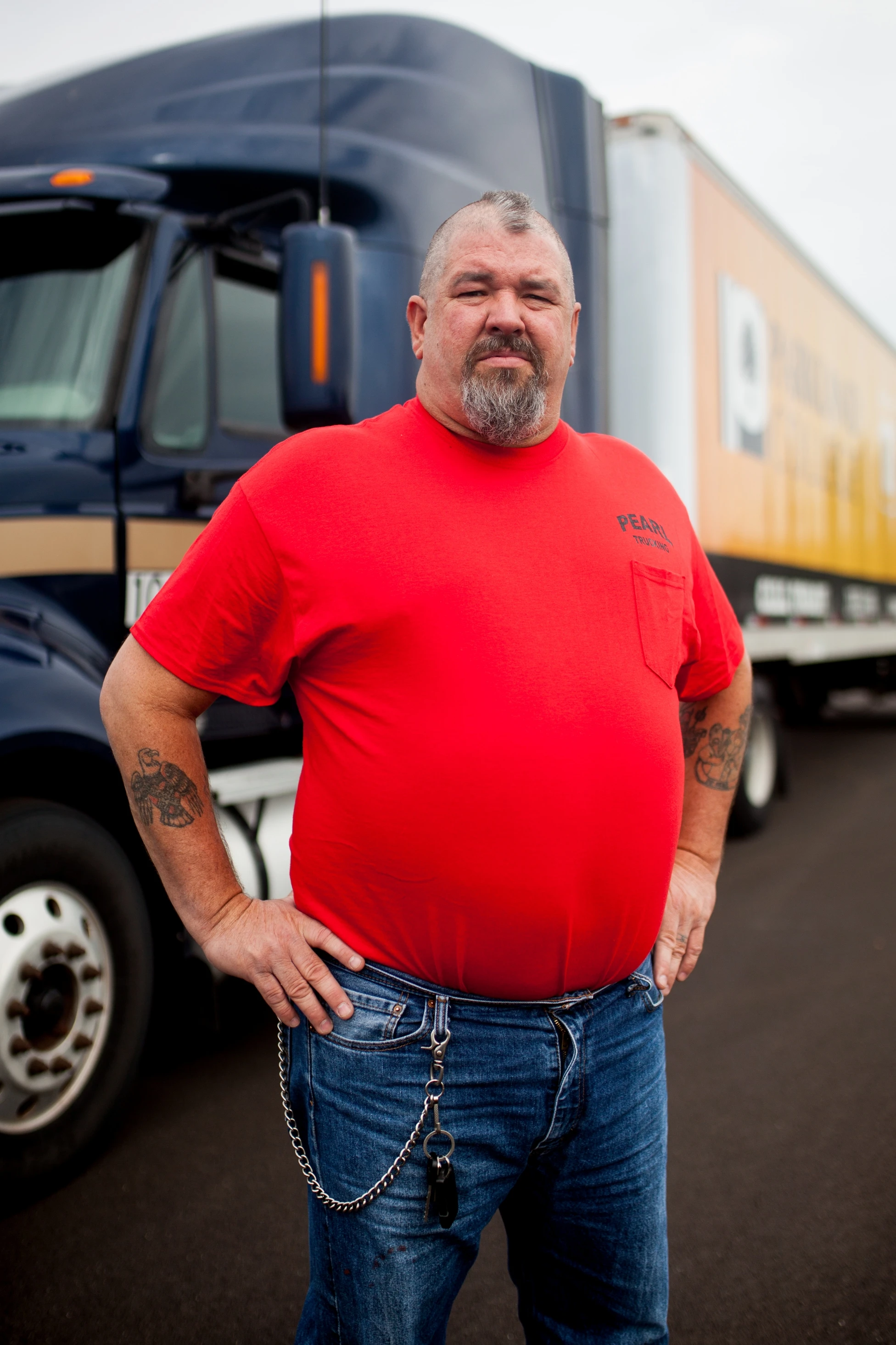 A man in a red shirt standing in front of a semi truck.