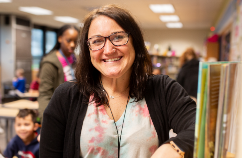 A teacher smiling in the hallway of a school.