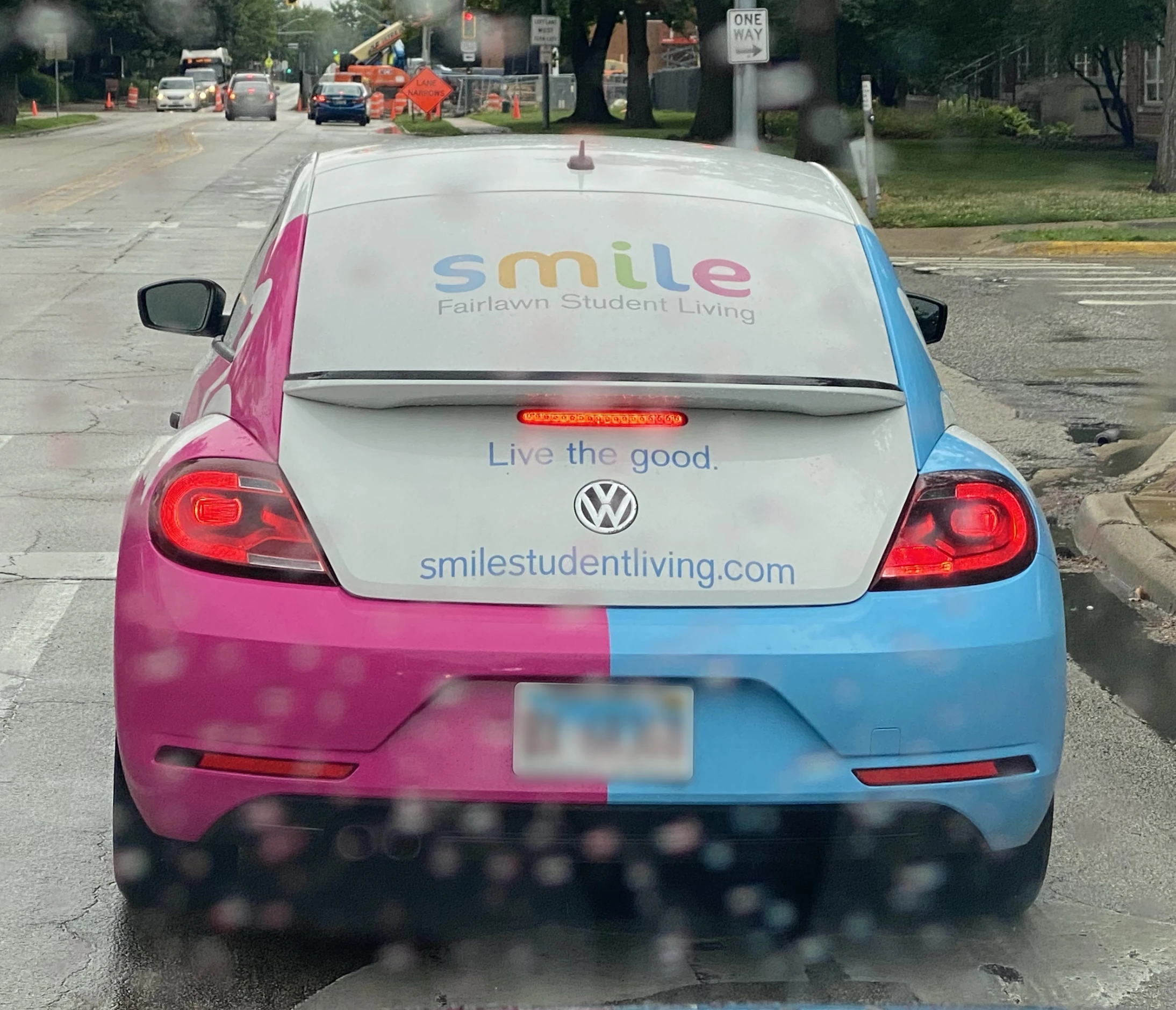 A pink and blue volkswagen beetle is driving down the street.