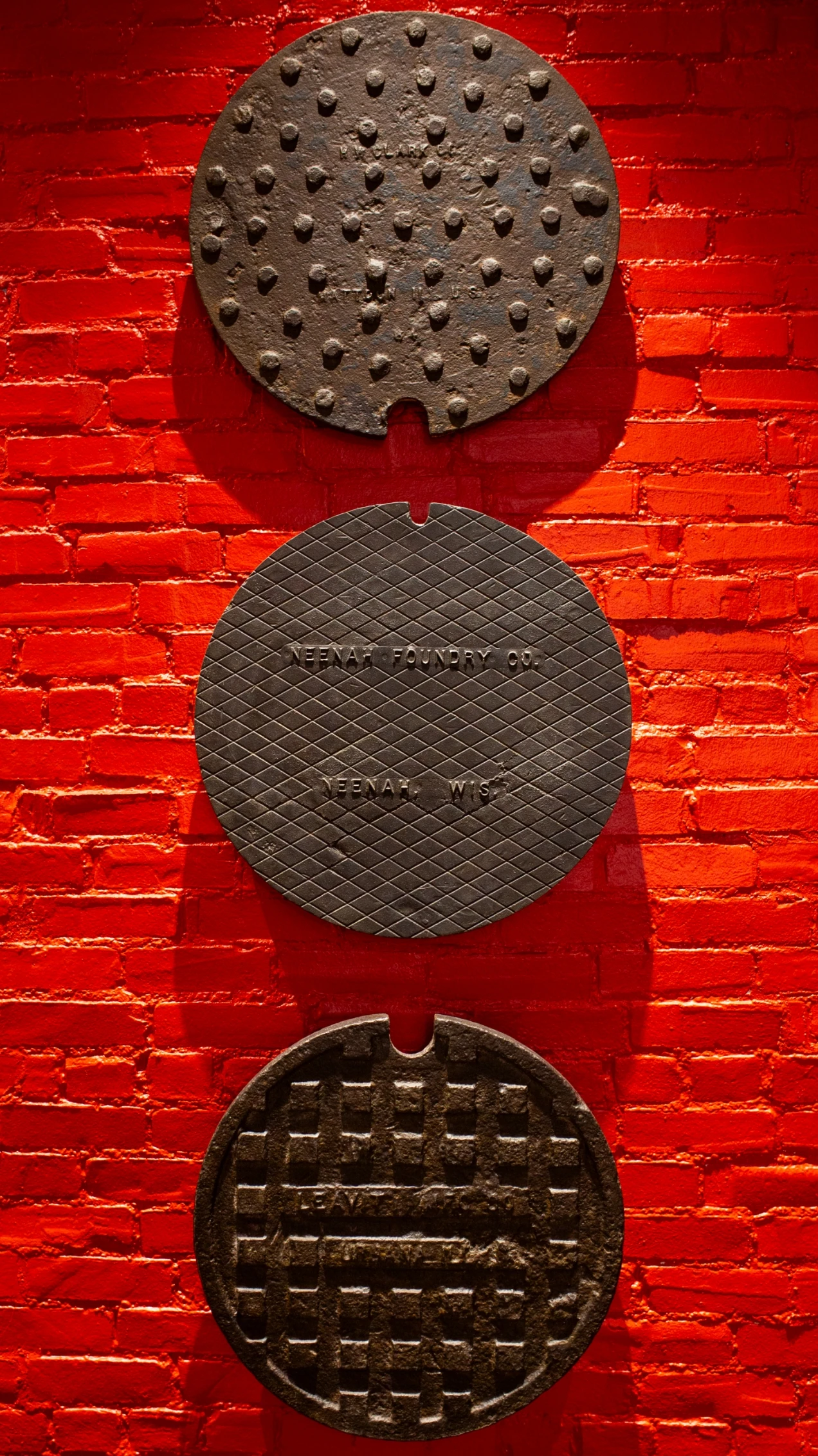 Three manhole covers hanging on a red brick wall.